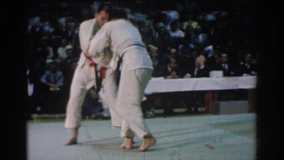 Close spectator view of two competitors grappling in white gis on a green mat at the 1966 West Covina event.