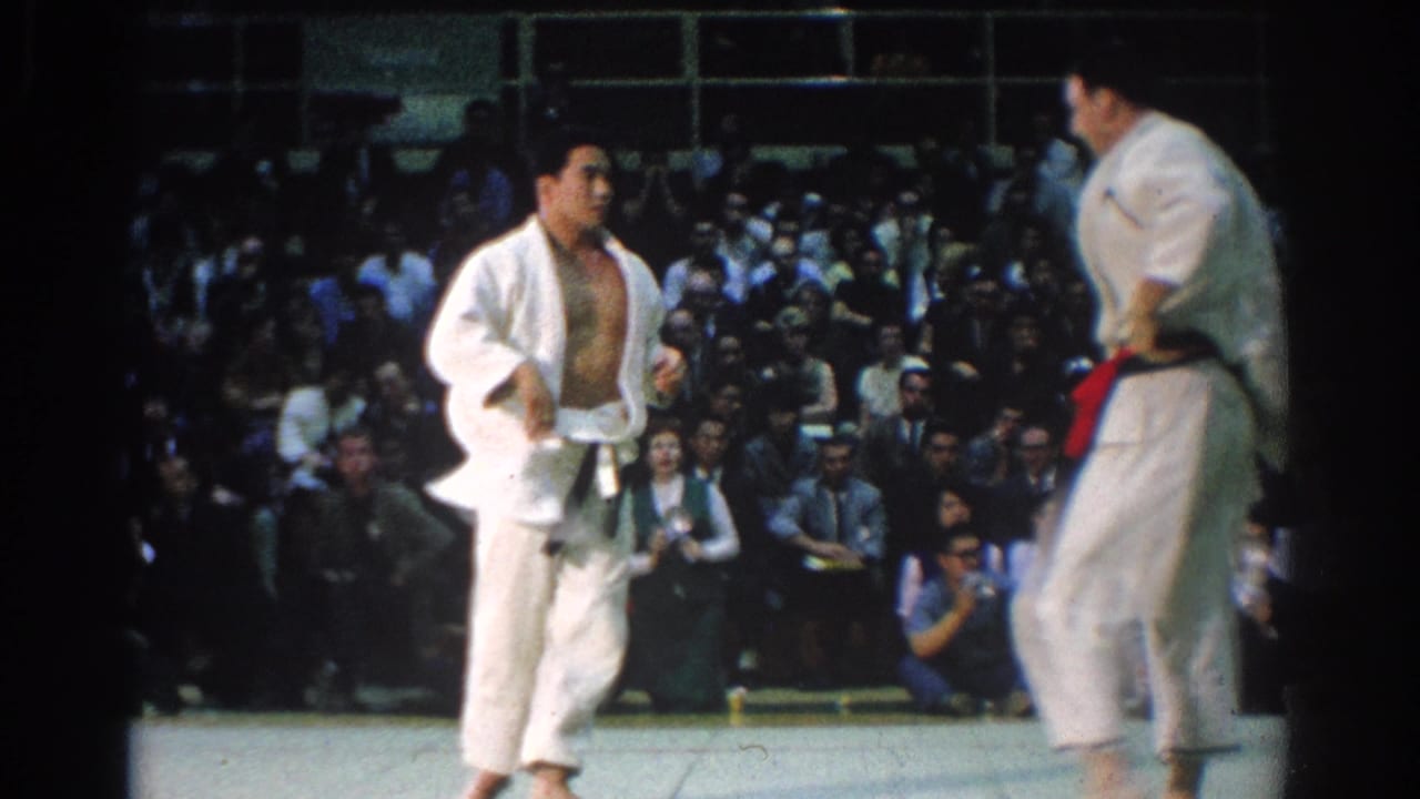 The competitors appear to reset during the 1966 West Covina judo match, one with an open gi jacket and another at frame right wearing a red belt.