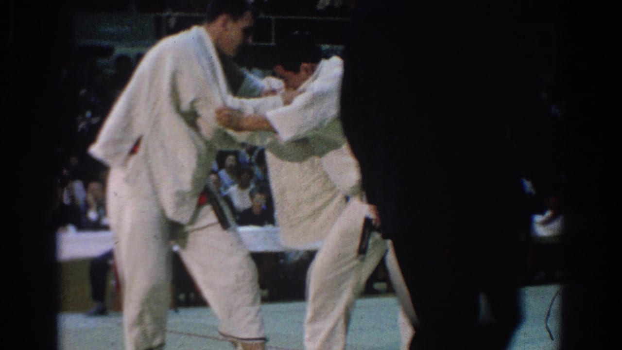 Two men in white gi, one with a visible red belt, grapple closely during the 1966 West Covina karate tournament.