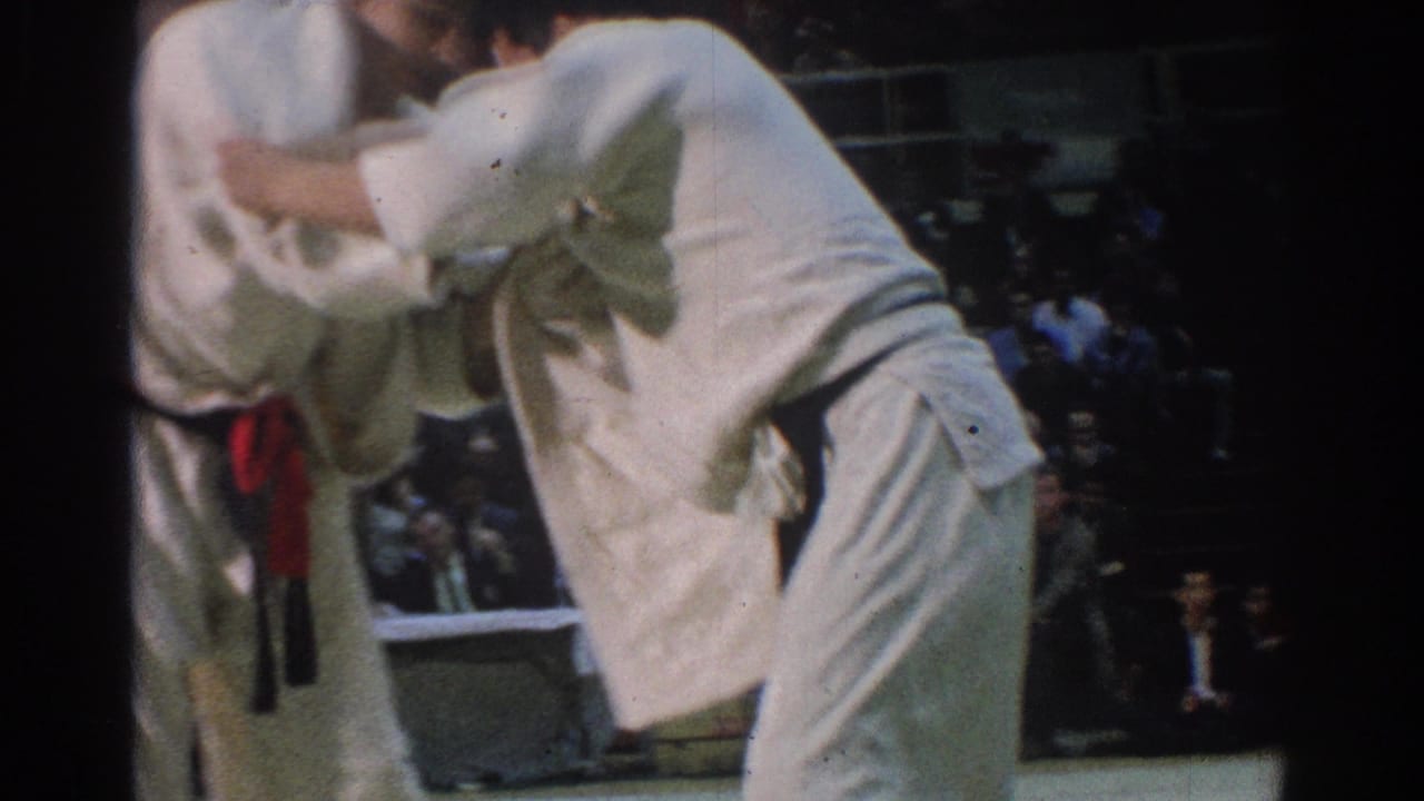 A close 8mm frame shows one judoka bent forward as both competitors hold lapel and sleeve grips in the West Covina match.