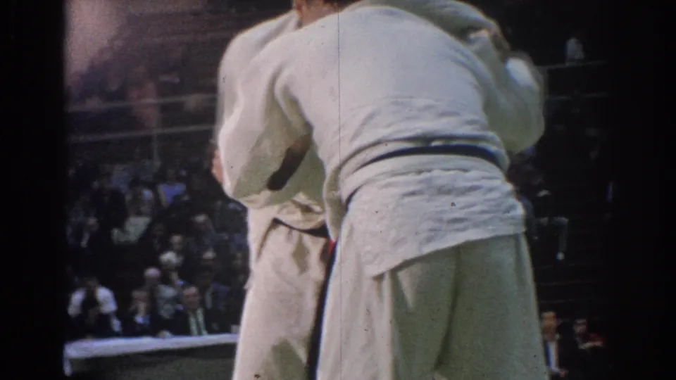 One martial arts competitor is seen from behind while grappling with another athlete in a 1966 indoor West Covina match.
