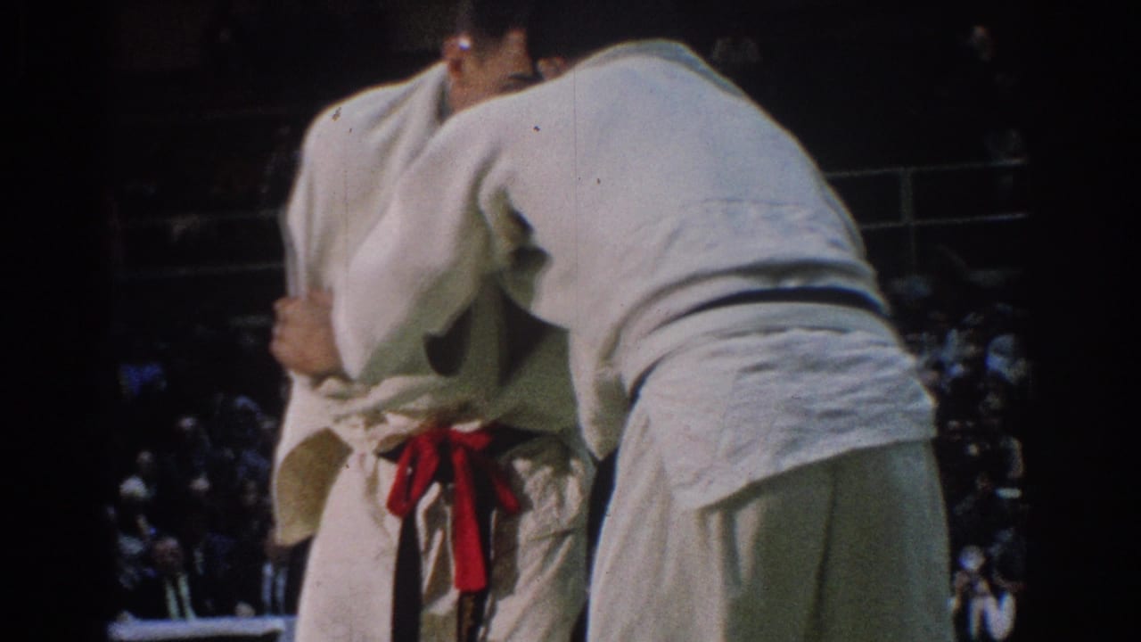 Two men in white gi continue a tight grappling exchange during the 1966 West Covina match, with the red belt visible at center.