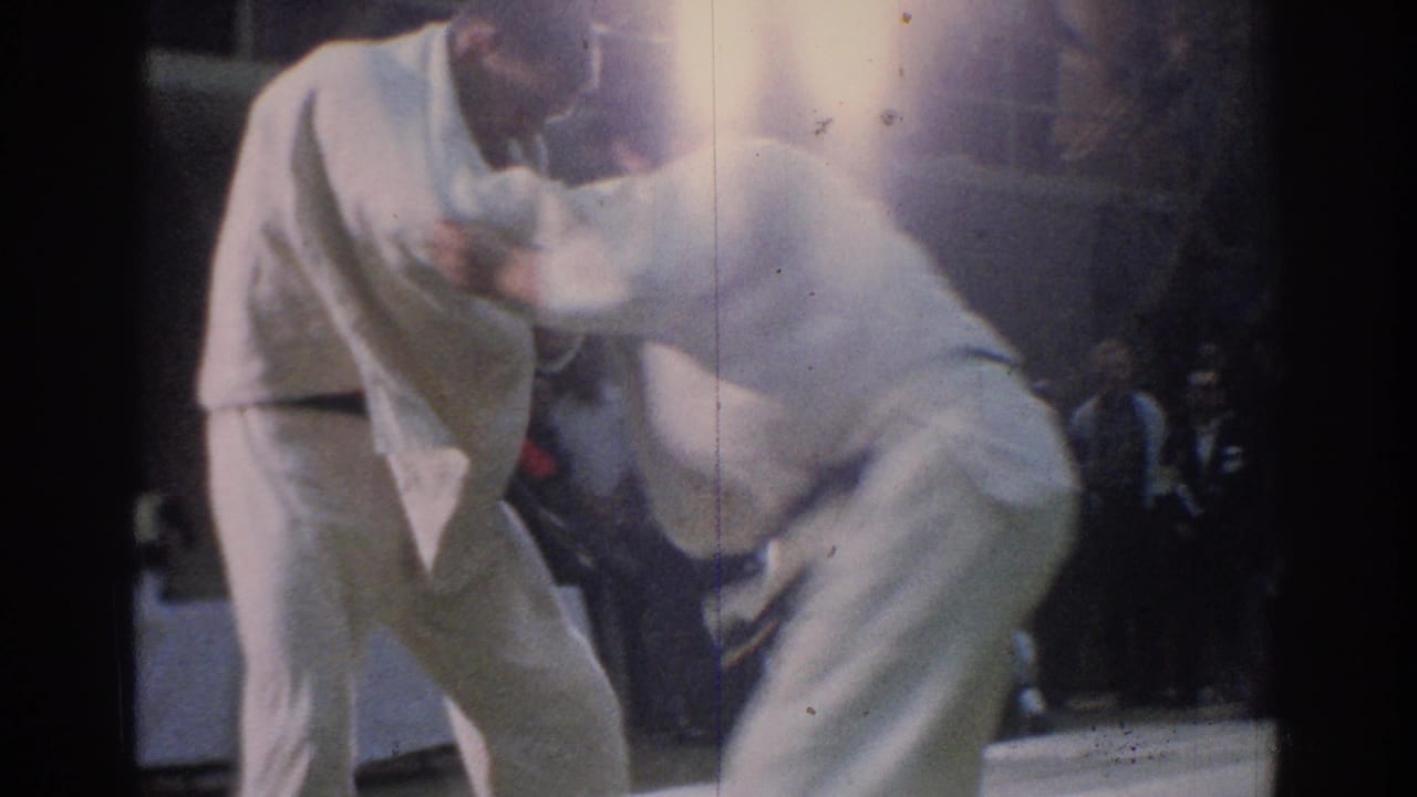 Two adult karate competitors in white gi grapple at close range during an indoor match.