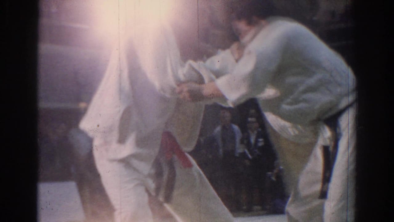 A close 1966 West Covina karate frame shows two adult competitors in white gi grappling under strong light flare.
