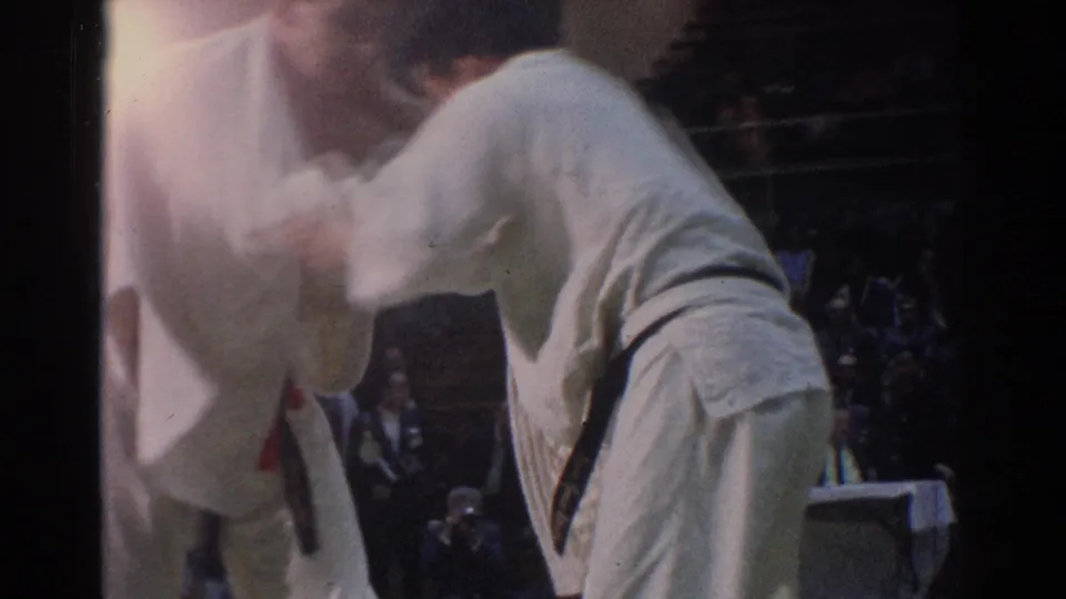 Close 8mm footage from West Covina, 1966 shows adult karate competitors pressing into a hold in front of a seated crowd.