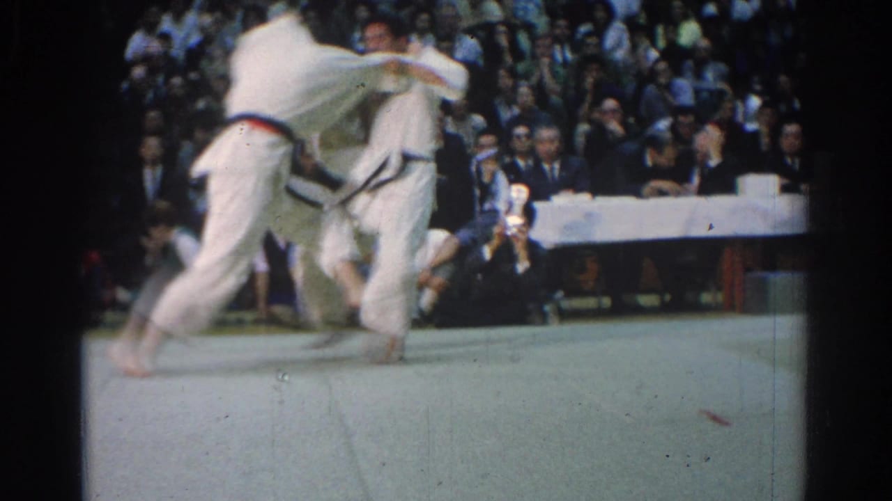 Two judokas move through a standing throw with a crowded audience behind them.