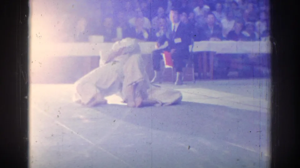 A flared 8mm frame shows two judokas on the mat during the match, with the audience softened by exposure and color shift.