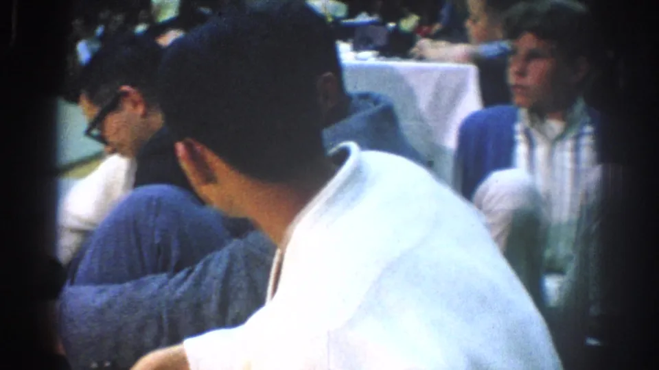 A close handheld frame shows a white-gi martial artist seated near spectators during the 1966 West Covina indoor event.