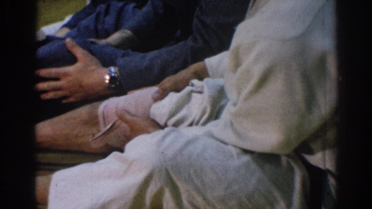Close view of a robed seated person while another adult holds a bare foot.