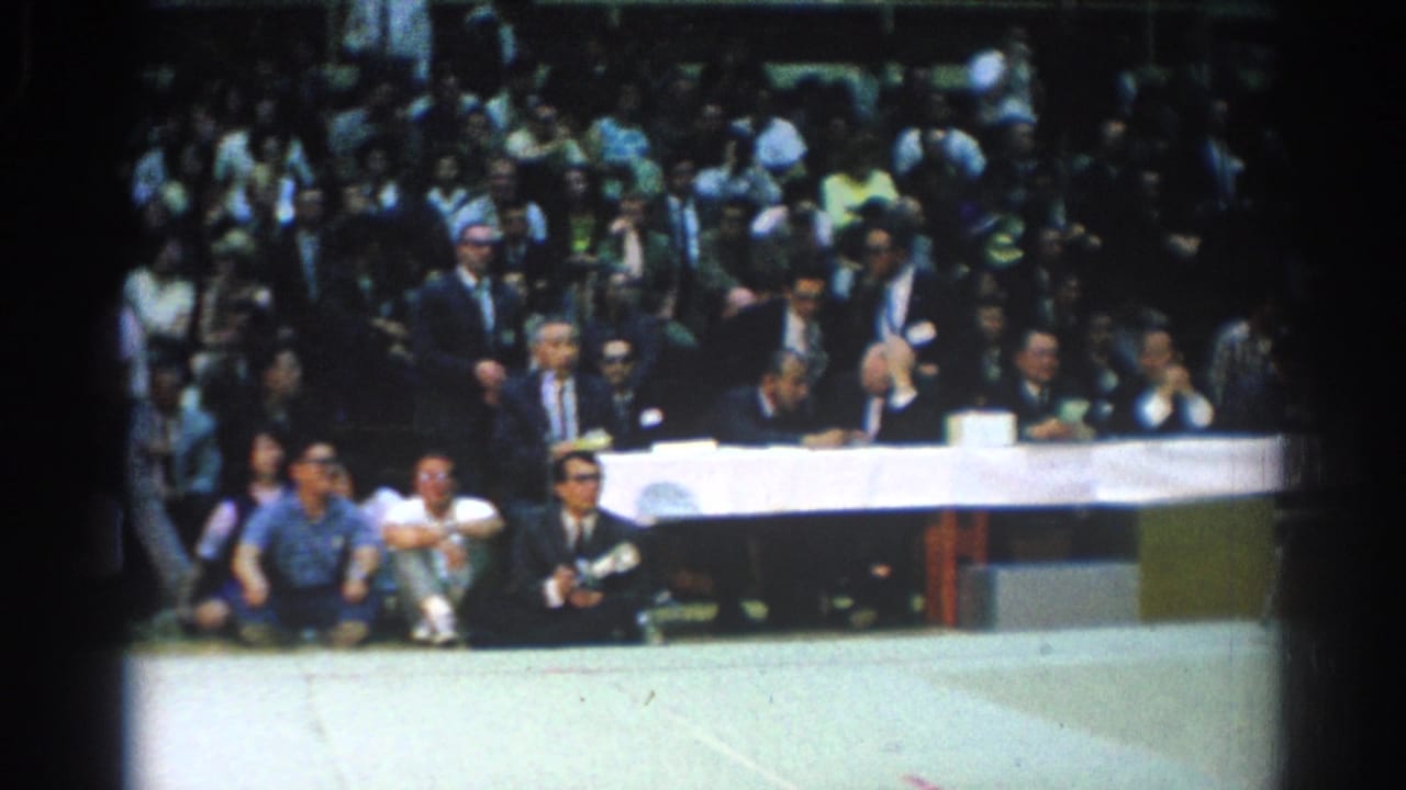 A long white-clothed officials table sits before a crowded spectator section at the 1966 West Covina indoor event.