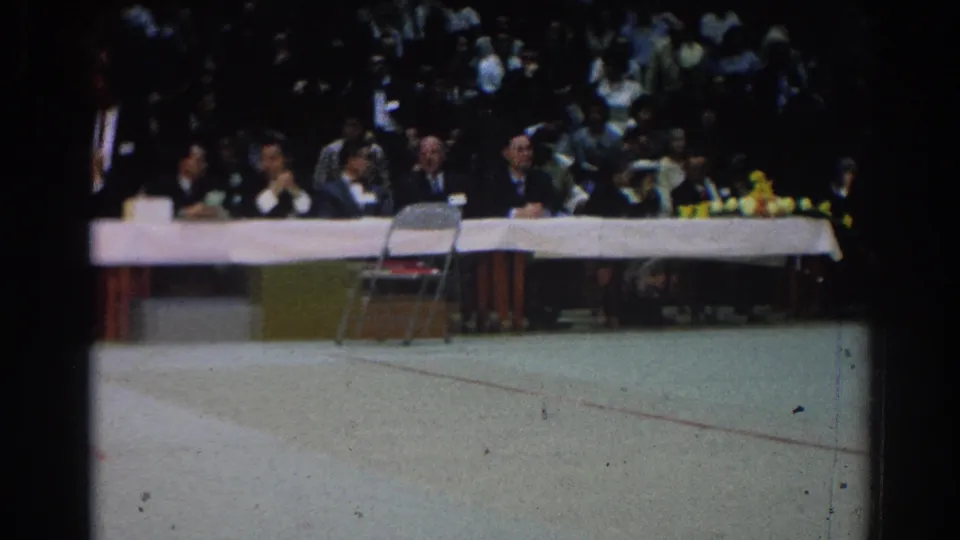 The 8mm frame shows a crowded indoor West Covina event with suited officials seated at a long table in 1966.
