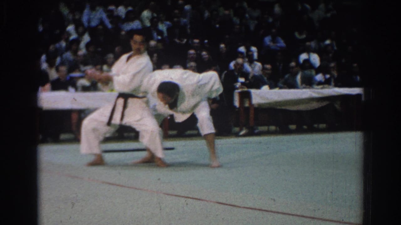 A black-belt competitor controls another martial artist during a throw sequence on a green competition mat.