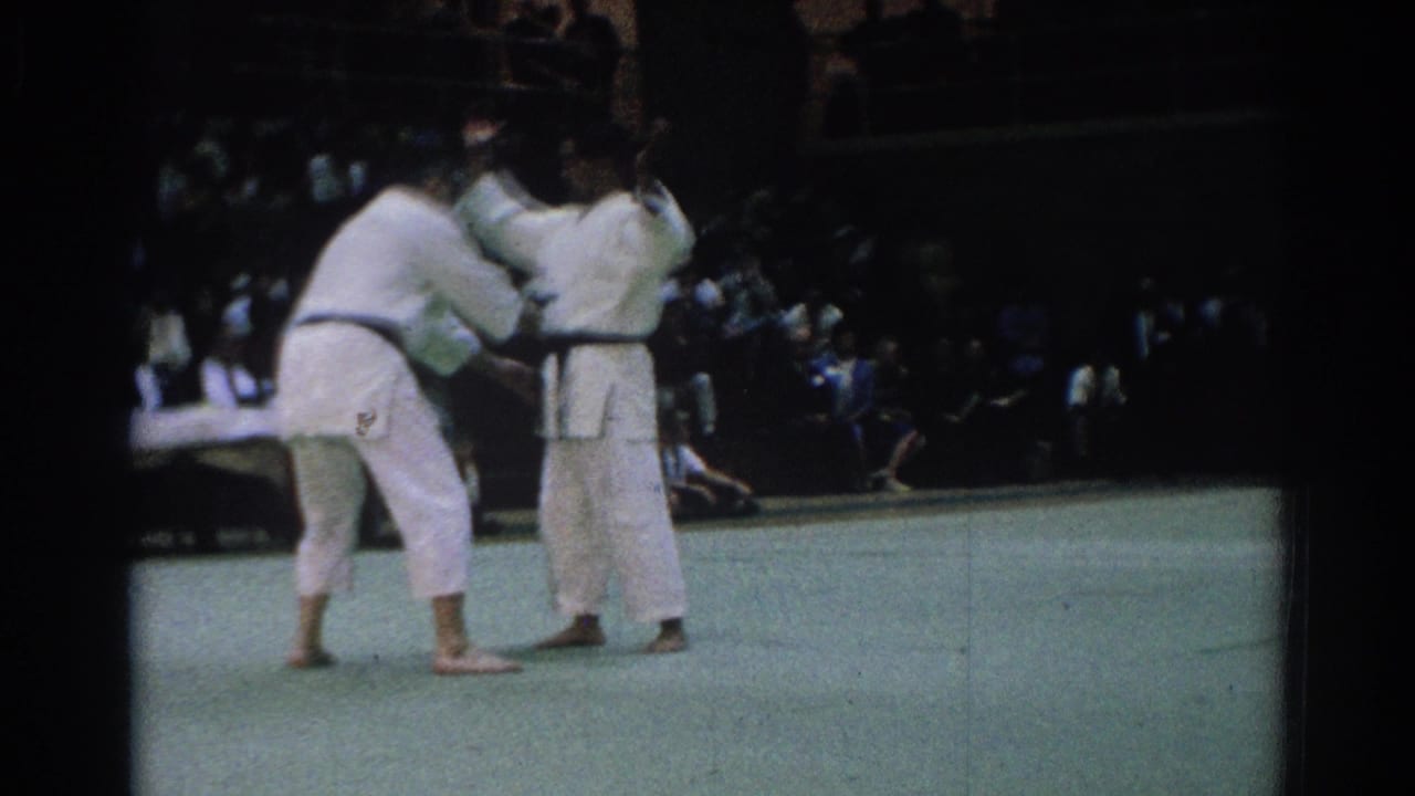 Two adult martial artists in white gi and dark belts begin a judo grip sequence on a mat in 1966 West Covina footage.