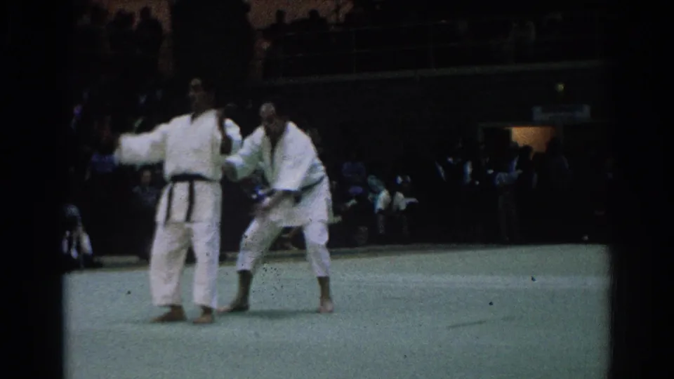 Two adult competitors in white gi face off on a green mat in the West Covina indoor martial arts scene.