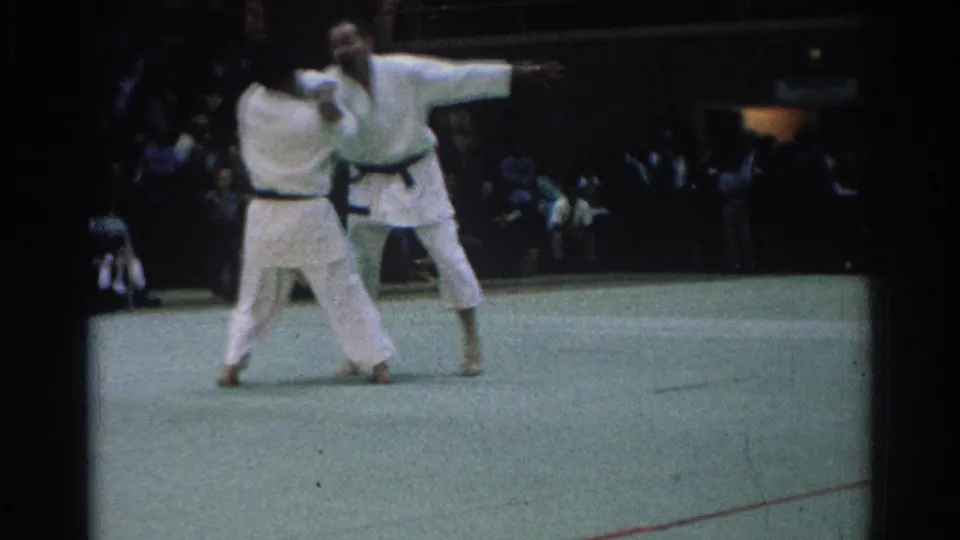 During the 1966 indoor match, one martial artist extends an arm while the other holds close on the green mat.