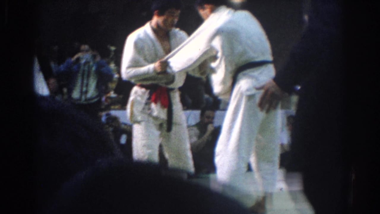 1966 West Covina frame with two judo competitors facing each other under indoor lighting, with audience members in the background.