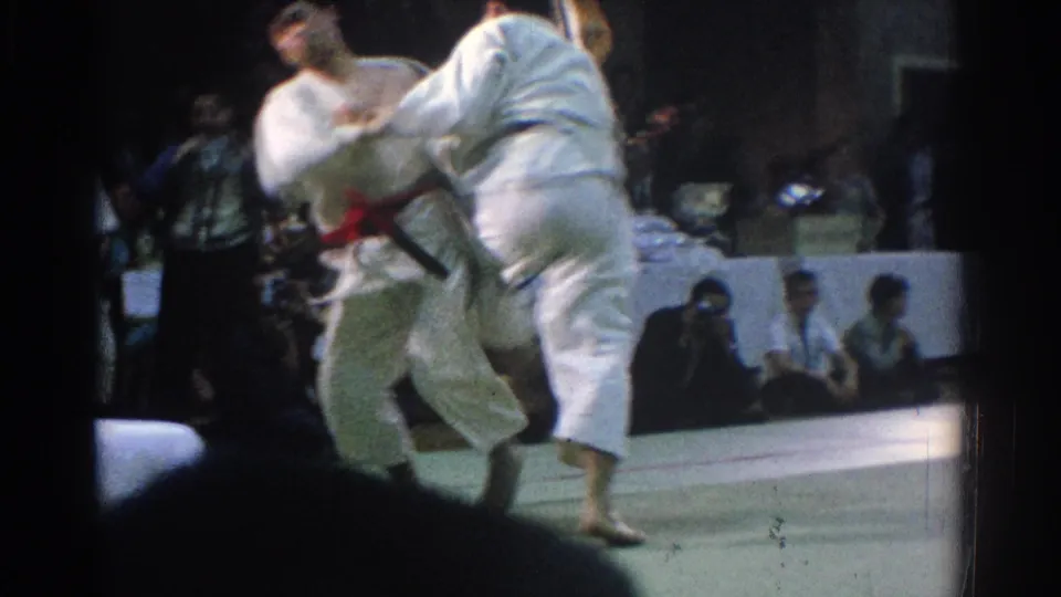 1966 West Covina 8mm frame capturing a dynamic judo throw attempt with spectators watching from the side of the mat.