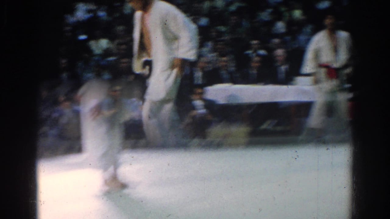 Two judo competitors in white gi move on an indoor mat during a 1966 West Covina match, with spectators in the background.