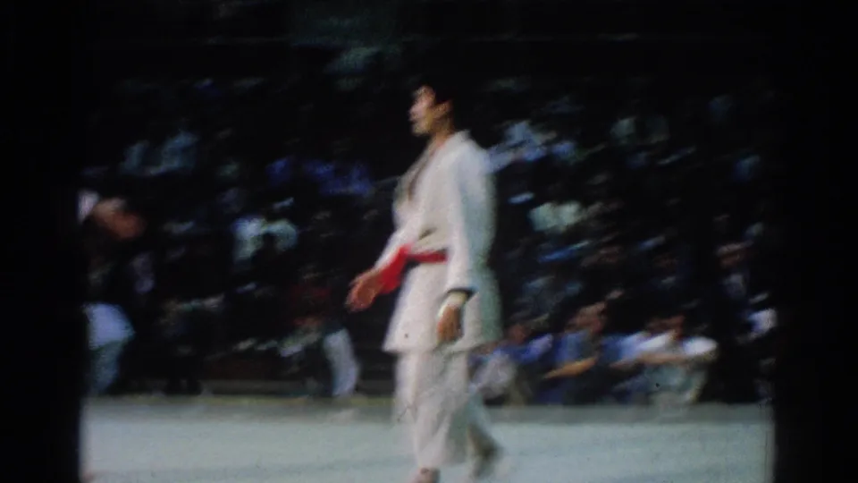 A red-belt judo competitor in a white gi walks across the mat during the West Covina 1966 indoor match.