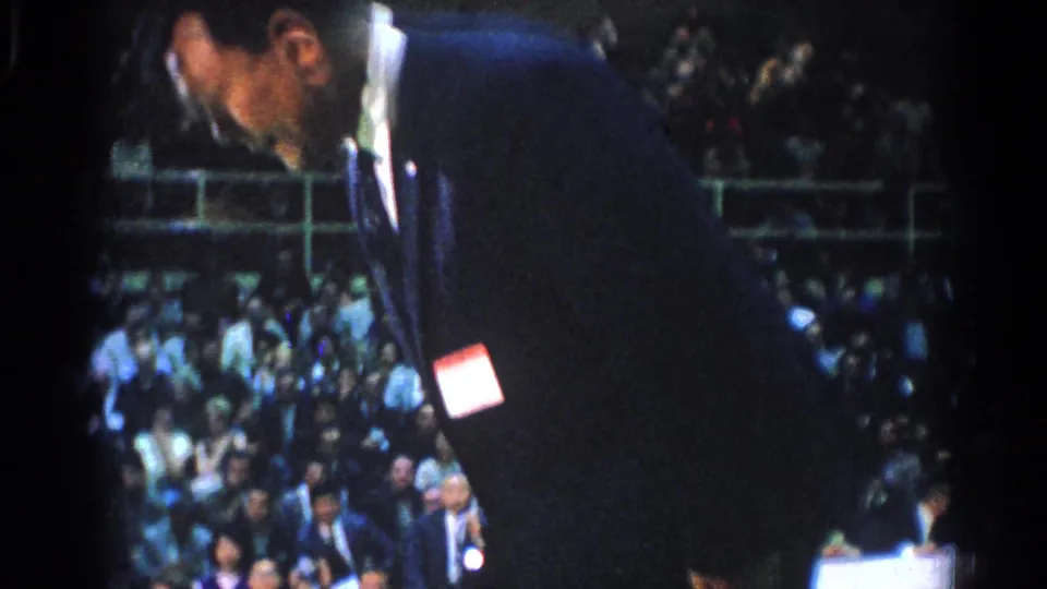 A dark-suited referee leans forward near the competition area while spectators fill the bleachers in this 1966 West Covina karate scene.