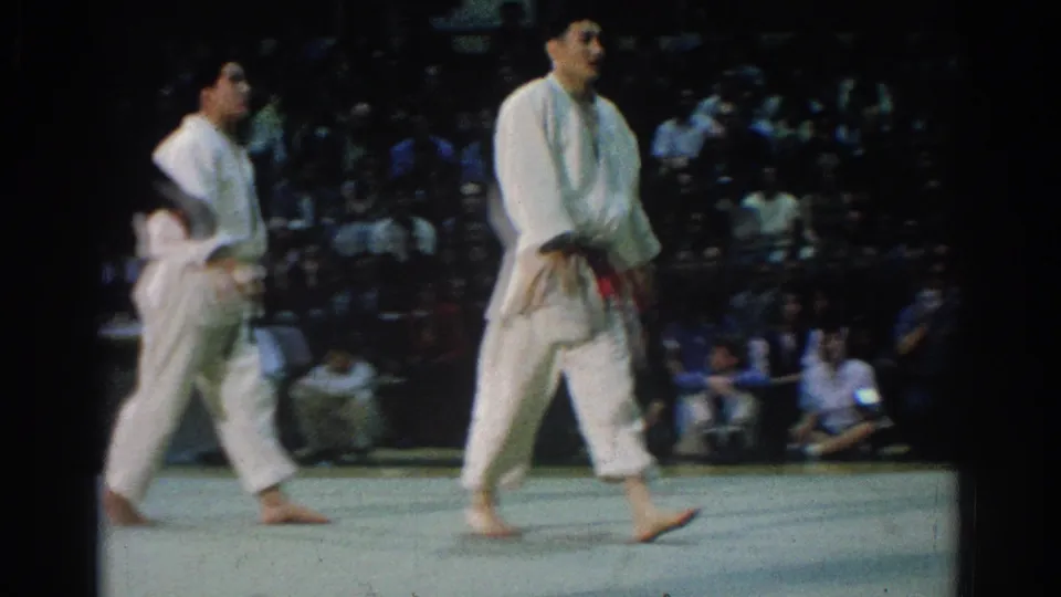 At the end of the 1966 West Covina judo clip, the competitors walk across the indoor mat while the audience remains visible behind them.