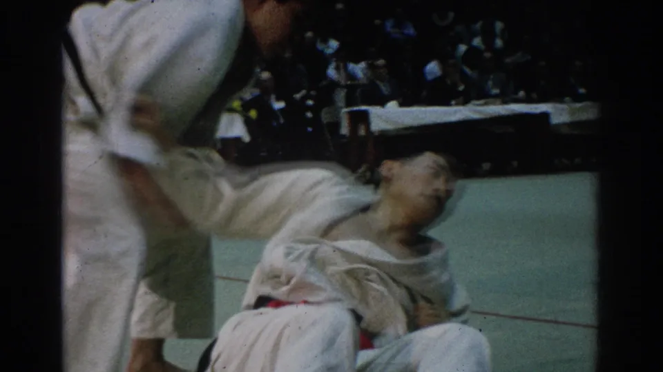 After a throw in the 1966 West Covina match, one judo competitor is down on the mat while the other remains standing nearby.
