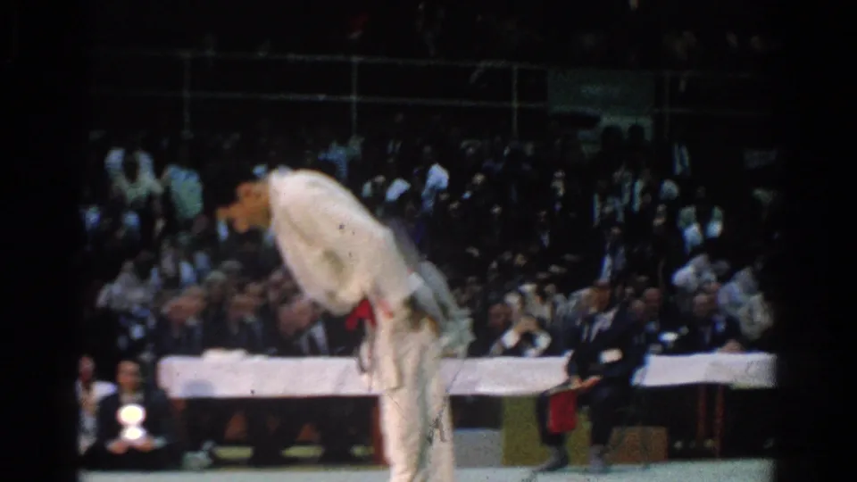 A white-gi practitioner with a red belt bows before judges and spectators at the 1966 West Covina tournament.