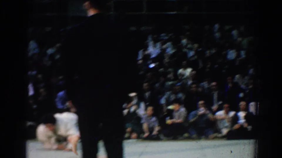 1966 West Covina judo match frame with the referee partly blocking the view as competitors remain low on the mat.