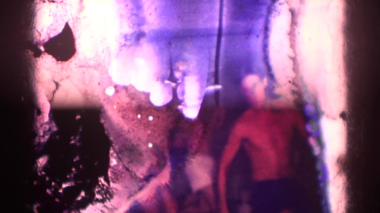 Damaged film frame with a blurred shirtless man standing in a dim interior.