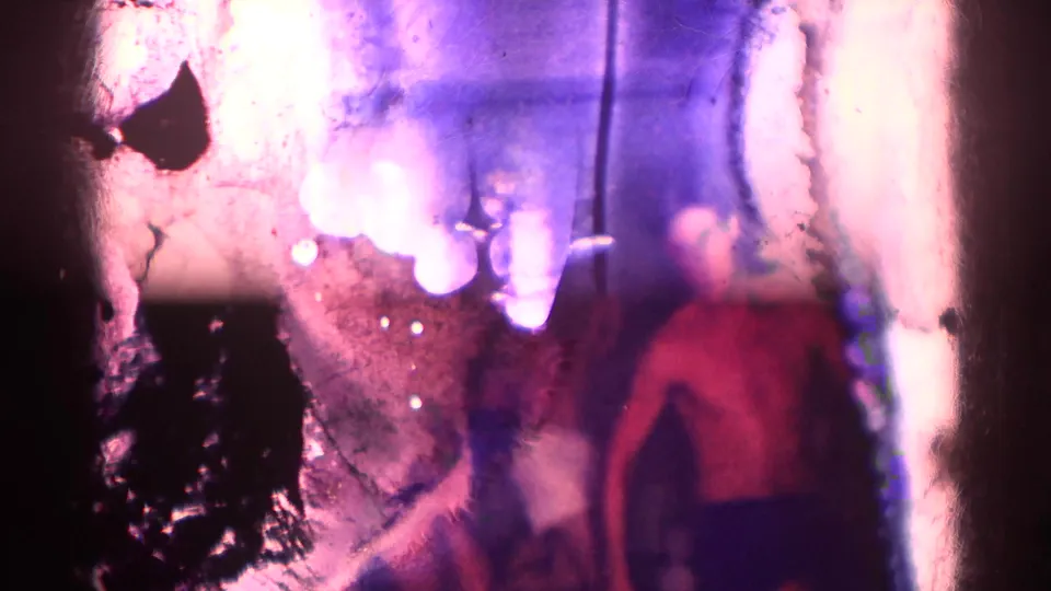 1967 Los Angeles 8mm frame with heavy film damage and a blurred adult man standing in a dim private interior.