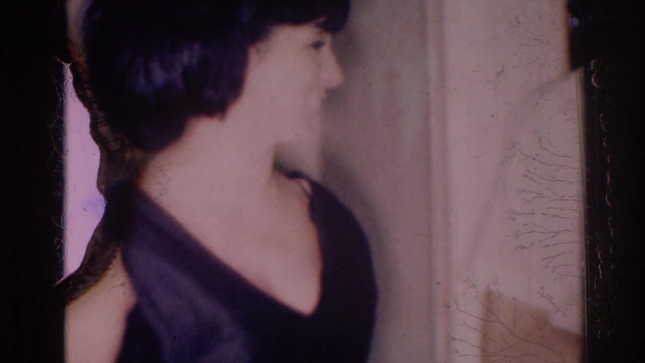 Woman with short dark hair in a dark dress seen in profile indoors.
