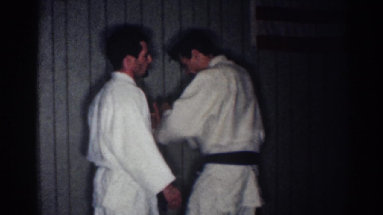 A black-belt instructor gestures near another man's hands during karate practice.