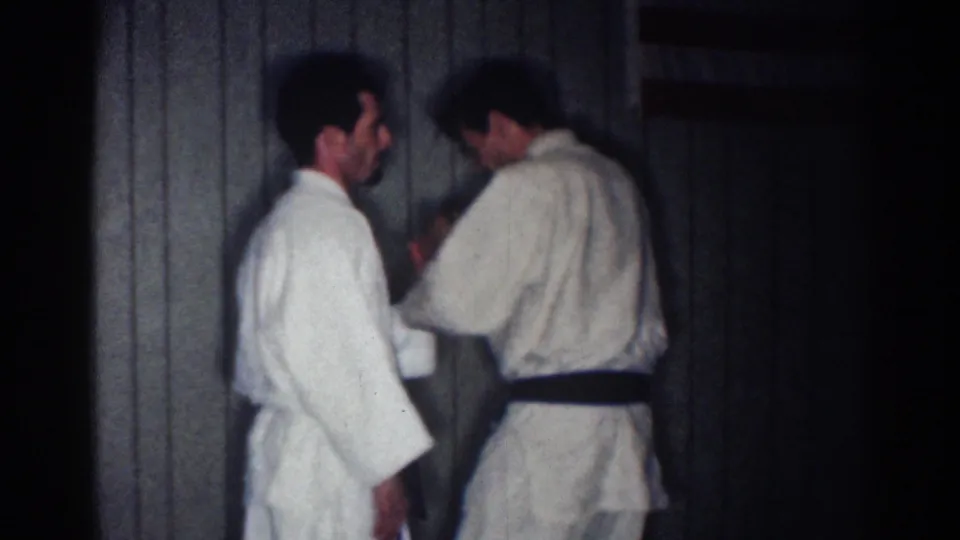 1967 Los Angeles indoor training frame with two adult men in white gi, one wearing a black belt and working through a hand technique.