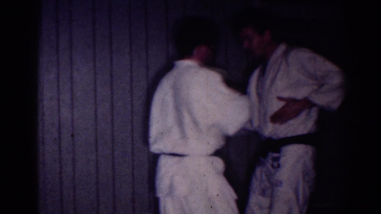 A man in a white uniform reaches toward another man wearing a black belt.