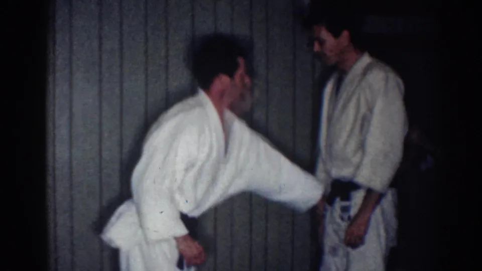 A white-uniformed practitioner extends an arm toward a black-belted partner in the final frame of the 1967 Los Angeles home movie.