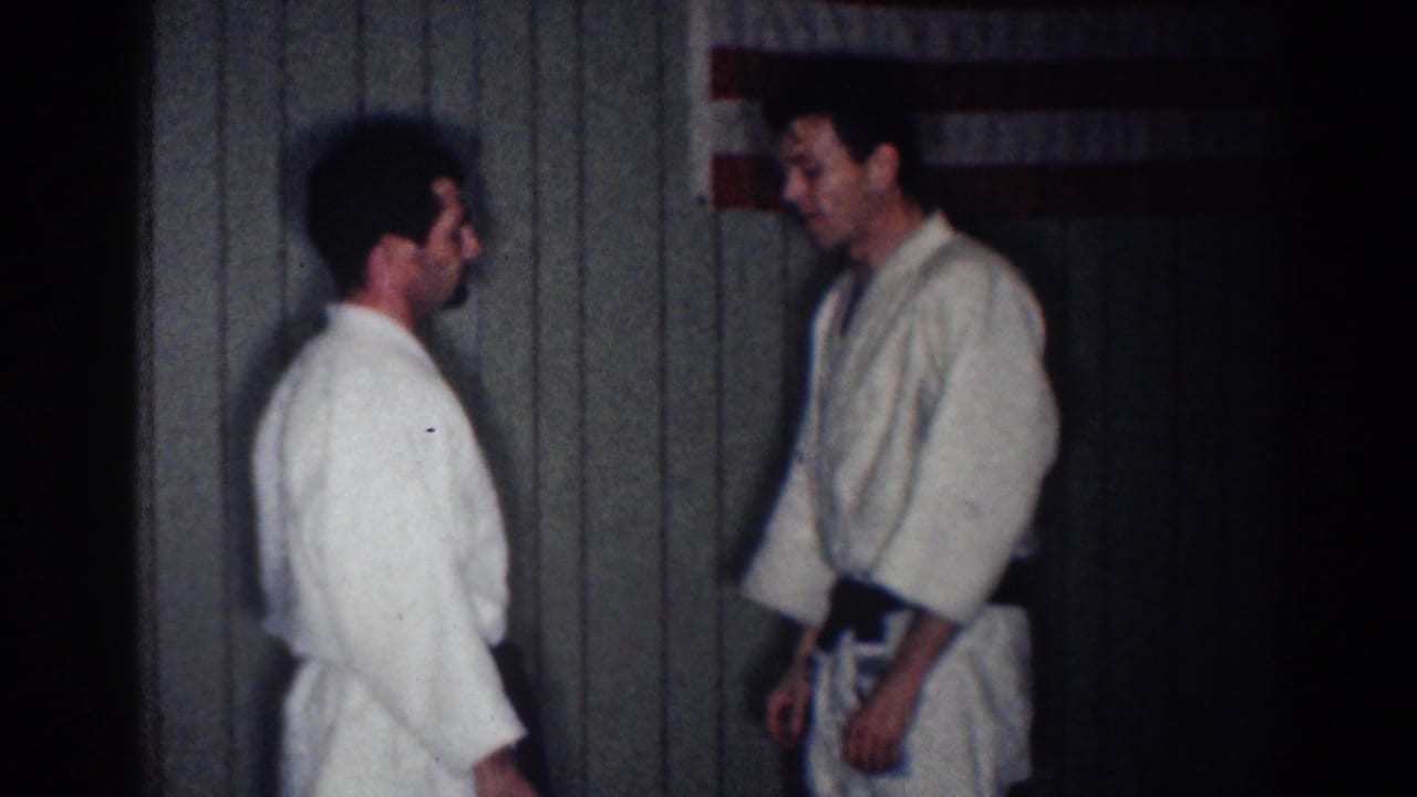 Two men in white gi stand facing each other near an American flag.