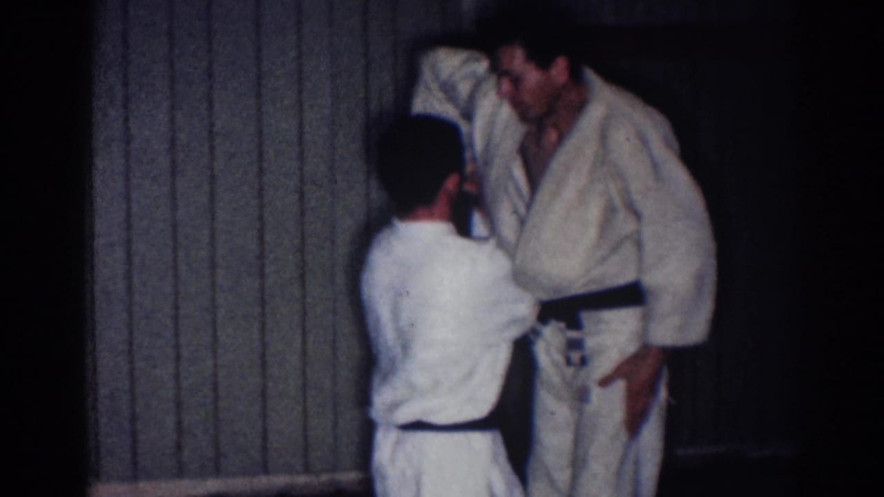 A shorter athlete reaches toward a taller athlete in a white gi during a judo demonstration.