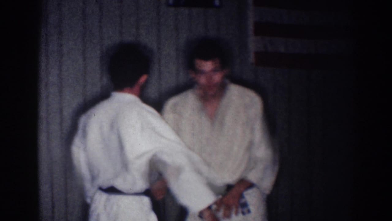 One man reaches toward another man in a white gi during martial arts practice.