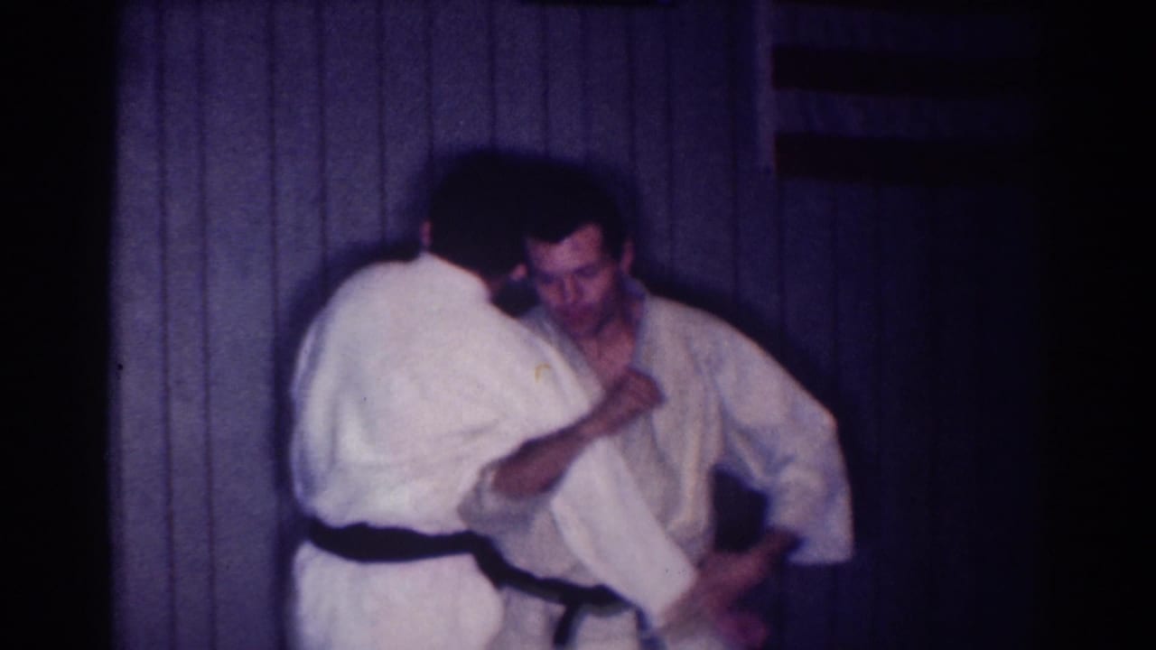 In supported 1967 Los Angeles home-movie footage, two adult men in white gi practice close-range karate or martial arts grappling indoors.