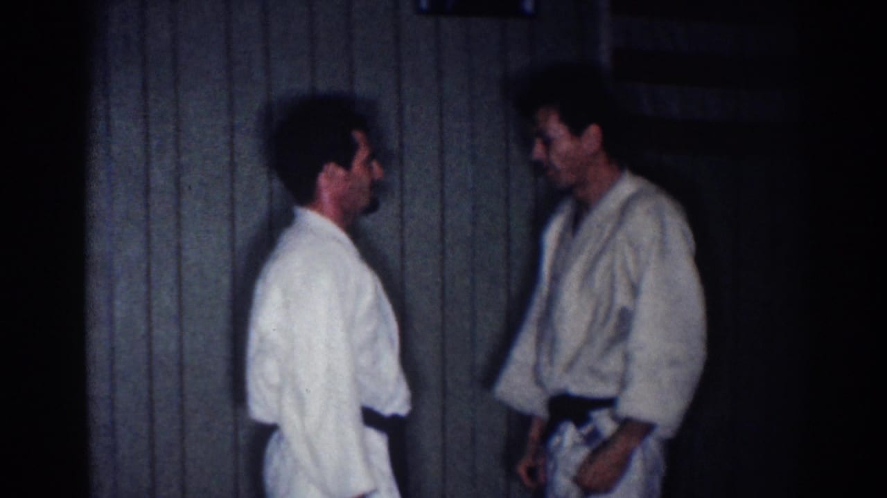 Two adult men in white martial arts uniforms face one another during a pause or reset in the supported 1967 Los Angeles footage.