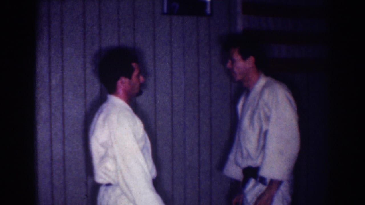 Two men in white gi face each other in a dim wood-paneled room.
