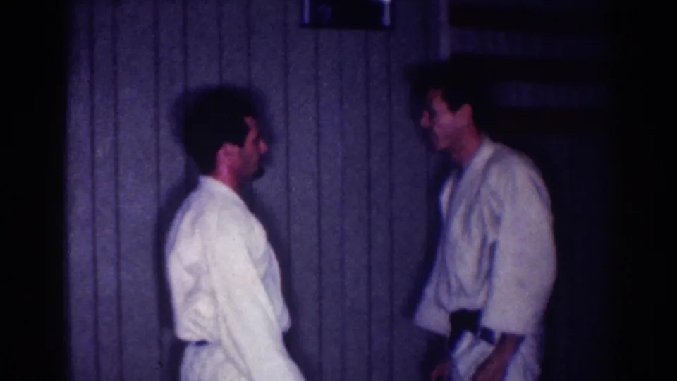 In 1967 Los Angeles home-movie footage, two adult men in white karate gi stand facing each other indoors.