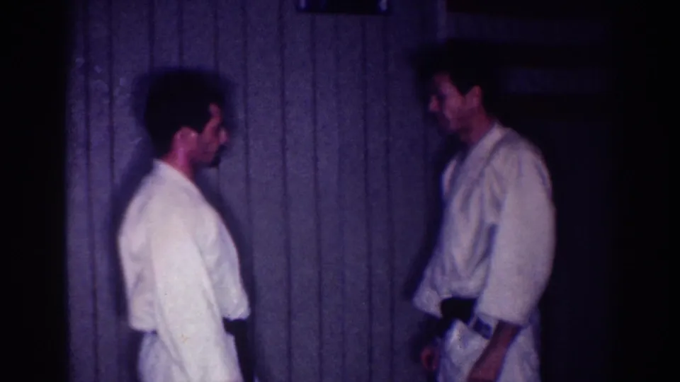 Two adult men in white gi and dark belts face off in a dim interior identified by metadata as Los Angeles in 1967.