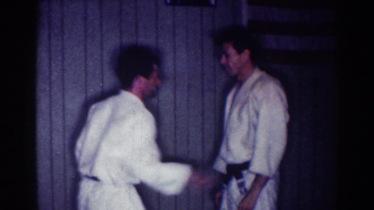 The partners face each other in the indoor 1967 judo practice footage, with motion blur from a quick arm movement.
