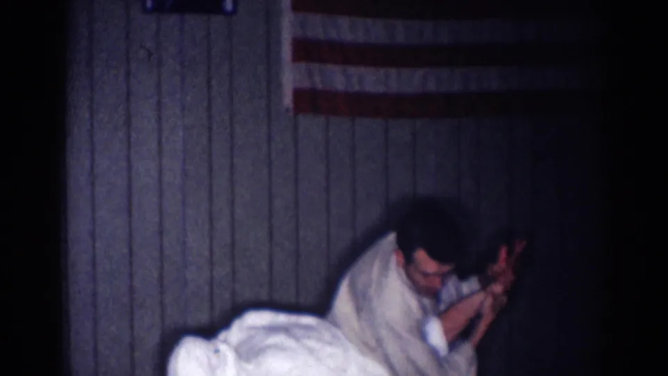 1967 Los Angeles karate practice frame showing two adult men engaged in a low grappling or hold movement indoors.
