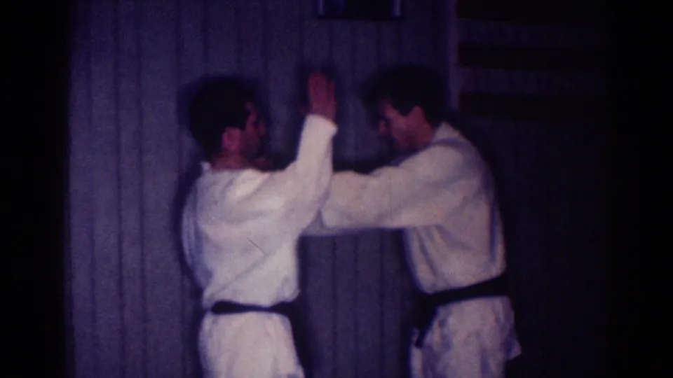 1967 Los Angeles frame of two adult men in white gi standing face to face during a martial arts practice movement indoors.