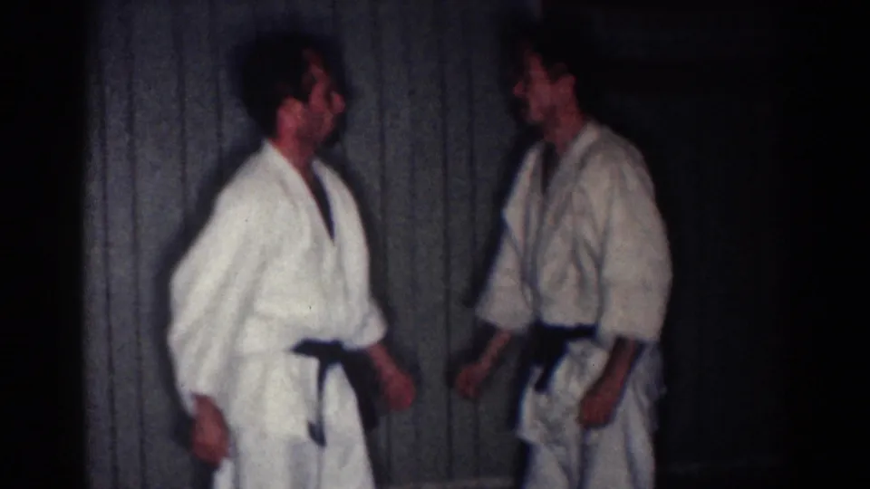 Two adult men in white gi and dark belts face each other indoors during the 1967 Los Angeles martial arts practice clip.