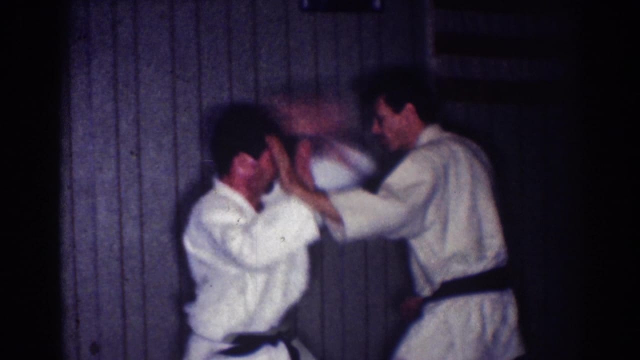 Two men in white judo uniforms and black belts raise their arms during indoor practice.