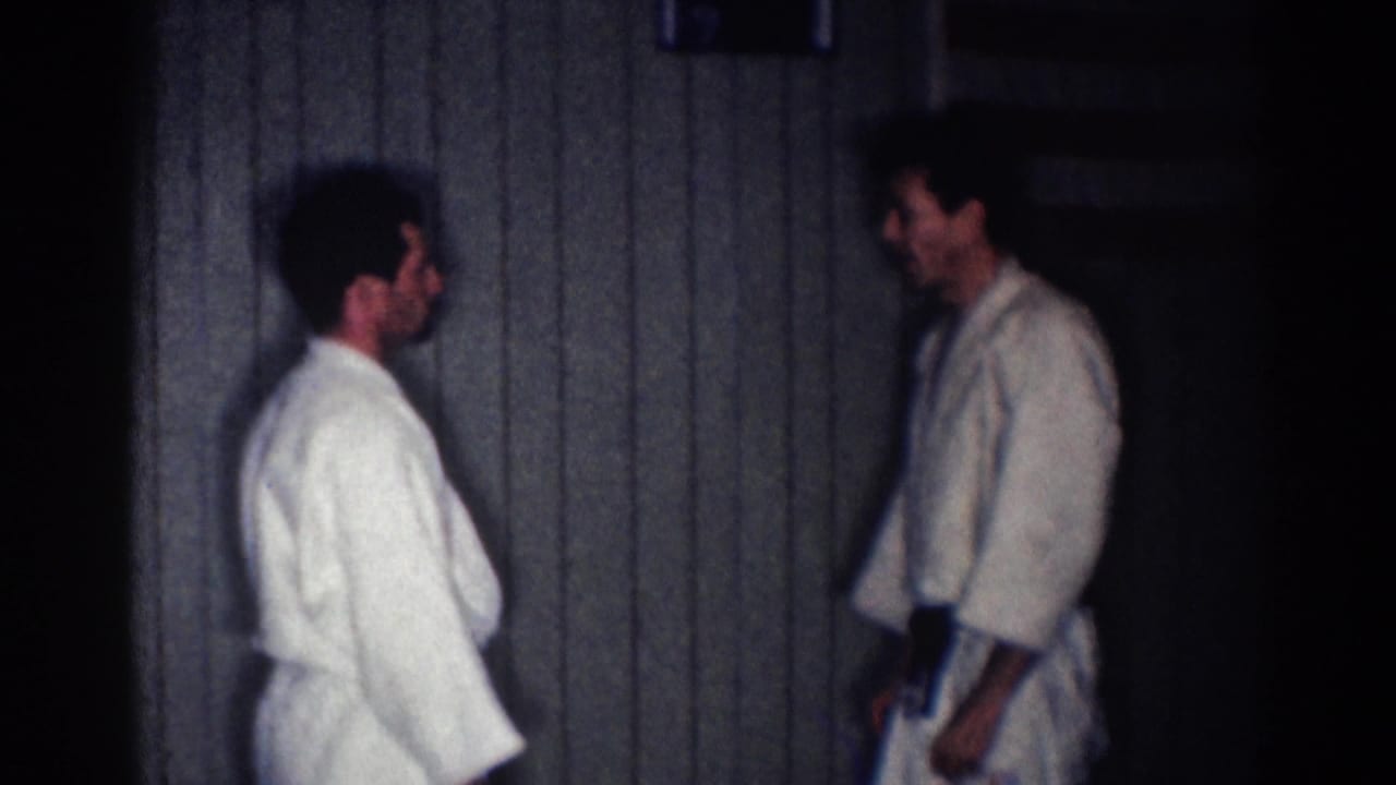 Two men in white karate uniforms face each other in a dim wood-paneled room.
