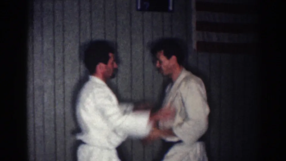 The two men continue a martial arts exchange, with motion blur from a quick hand technique in the dim 8mm frame.